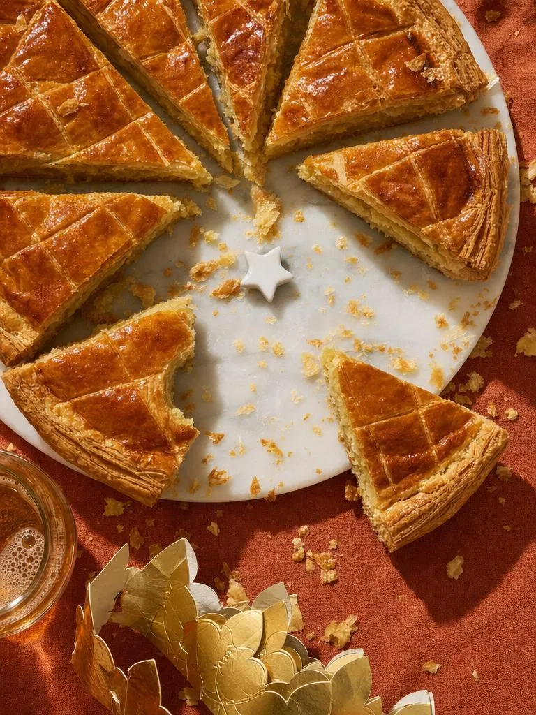 Galette des rois découpée sur nappe rouge, couronne dorée