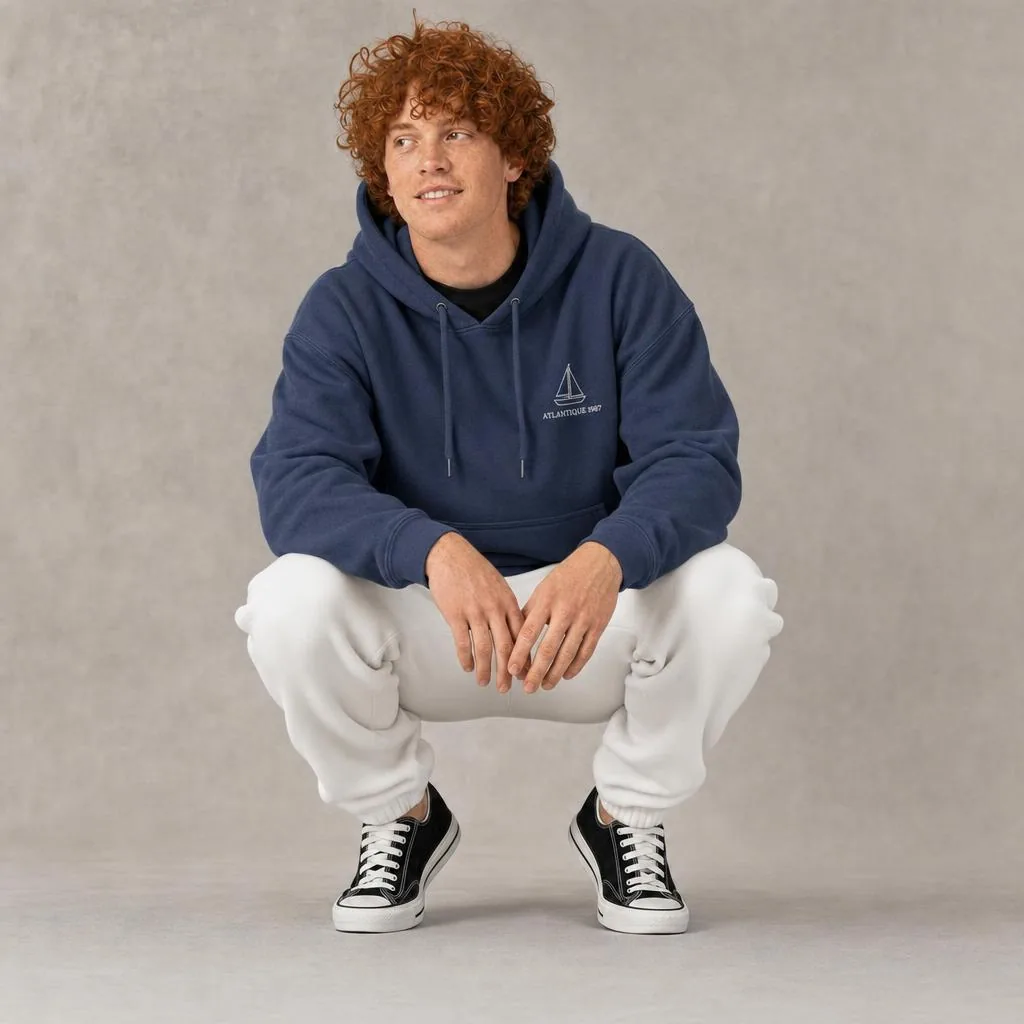 Hoodie marine et pantalon blanc, accroupi, fond neutre